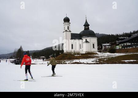 Seefeld, Österreich - Dezember 2022: Crosskrountry-Skifahrer (in Motion Blur) in der Nähe der Seekirchl-Kapelle (auch bekannt als Heiligkreuzkirche) in Seefeld Stockfoto