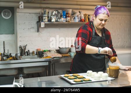 Konzentrierte weibliche Konditorin in schwarzer Schürze, die Desserts in der Bäckerei dekoriert. Professionelle Kücheneinrichtung. Hochwertiges Foto Stockfoto