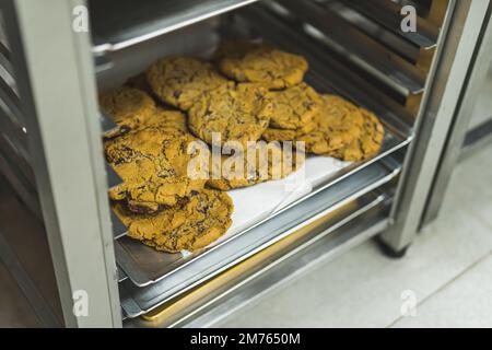 Leckere Kekse liegen auf dem Tablett in der professionellen Bäckerei Küche. Hausgemachte Schokoladenkekse auf Backpapier. Hochwertiges Foto Stockfoto