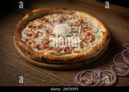 Köstliche Pizza mit Schinken, Zwiebeln und Spiegeleiern in der Mitte Stockfoto