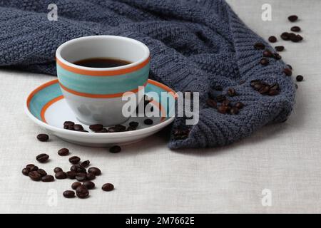 Eine bunte Tasse schwarzen Kaffees wird auf die Untertasse gestellt. Sowohl die Tasse als auch die Untertasse sind weiß mit orangefarbenen und aquafarbenen Ringen. Stockfoto