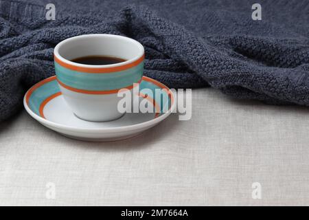 Eine bunte Tasse schwarzen Kaffees wird auf die Untertasse gestellt. Sowohl die Tasse als auch die Untertasse sind weiß mit orangefarbenen und aquafarbenen Ringen. Stockfoto