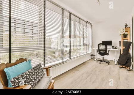 Ein Wohnzimmer mit Holzfußboden und weißen Fensterläden an den Fenstern mit Blick auf einen Büroschreibtisch Stockfoto