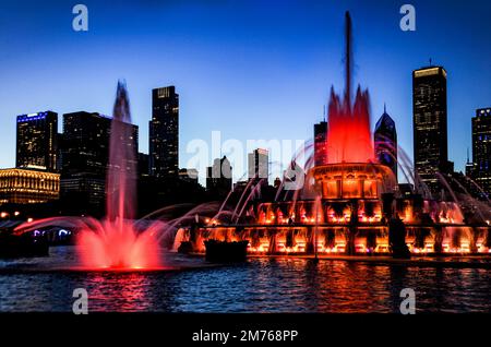 Der Buckingham Wasserbrunnen ist rot und goldfarben beleuchtet und bietet eine Show, während sich der Himmel in der Dämmerung in lila Silhouetten verwandelt, die die Skyline von Chicago prägen. Stockfoto