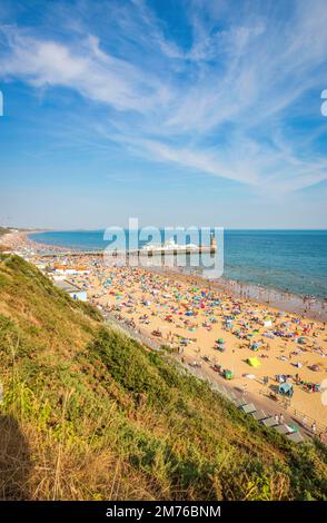 Blick auf Bournemouth Beach und Pier in Bournemouth Dorset UK bei Sonnenuntergang. Voller Strand im Sommer. Leute, die sich sonnen. Überfüllter Strand Stockfoto