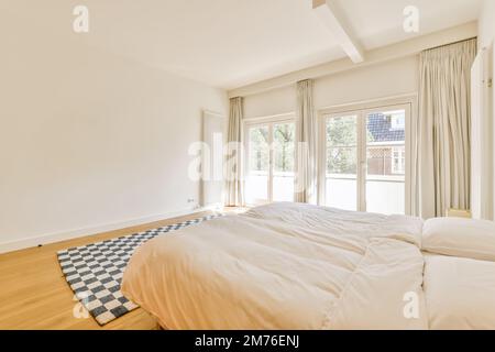 Ein Schlafzimmer mit weißen Wänden und Hartholzböden im mittleren Teil des Zimmers, es gibt ein großes Bett Stockfoto