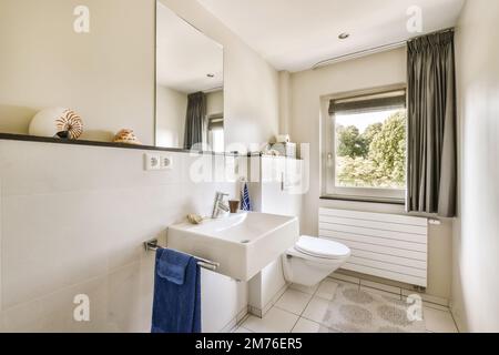 Ein Badezimmer mit Toilette, Waschbecken und Fenster auf dem Foto wird rechts gemacht, da hängen zwei Handtücher an der Stockfoto
