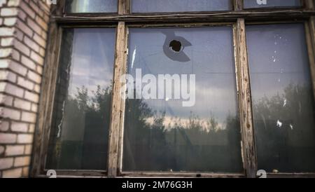 Ein Loch in der Fensterscheibe eines alten Hauses. Glas zerbrochen von Hooligans mit einem Stein Stockfoto