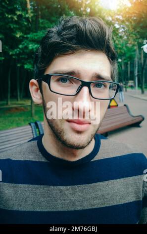 Ein junger Mann mit Brille steht auf der Straße und schaut auf die Stockfoto