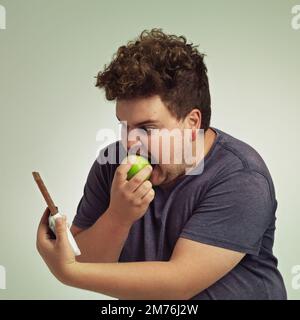 Der Versuchung entgehen - bleiben Sie bei Ihrer Diät. Ein übergewichtiger Mann, der einen Apfel beißt, während er eine Schokolade anschaut. Stockfoto