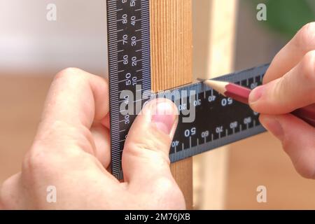 Zimmermann mit Zimmermannsquadrat, um die Linie des für die Bauarbeiten geschnittenen Holzes mit einem Bleistift zu markieren. Eine Nahaufnahme der Hände des Zimmermanns mit pe Stockfoto