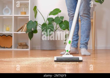 Reinigungsraum mit modernem kabellosen Staubsauger ohne Kabel. Ein Mann in Jeans saugt Sägemehl vom Boden mit einem modernen kabellosen Staubsauger. M Stockfoto