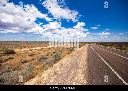 Auf der Straßenseite der Stuart-Autobahn. Entlang der verlassenen, unfruchtbaren, weiten Landschaft des australischen Outbacks. Der graue rote Asphalt schneidet durch das Design Stockfoto