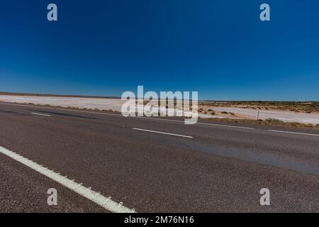 Auf der Straßenseite der Stuart-Autobahn. Entlang der verlassenen, unfruchtbaren, weiten Landschaft des australischen Outbacks. Der graue rote Asphalt schneidet durch das Design Stockfoto