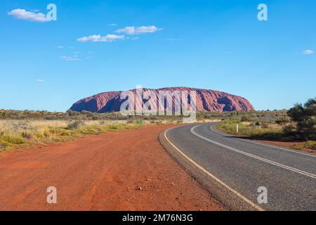 Outback, Australien - 12. November 2022: Straße zum berühmten Wahrzeichen des australischen Outbacks. Der rote Felsen des Uluru oder Ayres. Blauer Himmel Wüste la Stockfoto