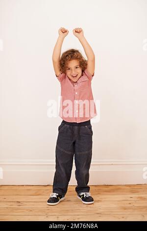 Ein Kind zu sein. Porträt eines aufgeregten kleinen Jungen, der seine Arme in die Luft hebt. Stockfoto