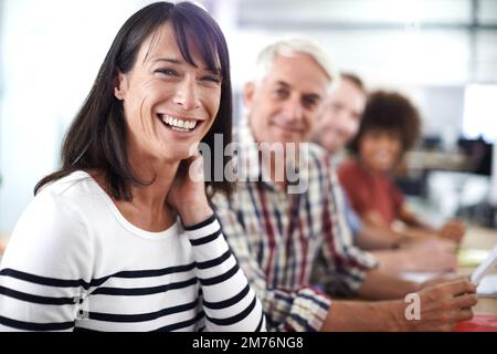 Wir sind ein tolles Team. Porträt einer attraktiven, reifen Geschäftsfrau, die mit ihren Kollegen an einem Tisch sitzt. Stockfoto