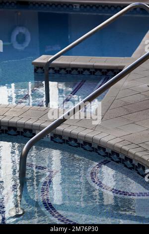 Poolfläche reflektiert Hochhaus der Stadt. Treppen und Geländer führen in kristallklares Wasser Stockfoto