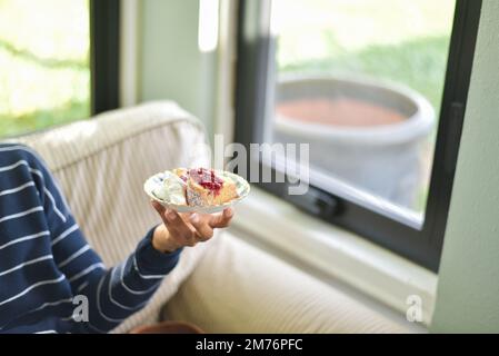 Eine Frau, die ein Stück hausgemachter Biskuitkuchen mit frischen Beeren und Schlagsahne in der Hand hält Stockfoto