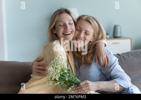 Fröhliche, friedliche, junge Tochter, die mama Blumen schenkt, Stockfoto