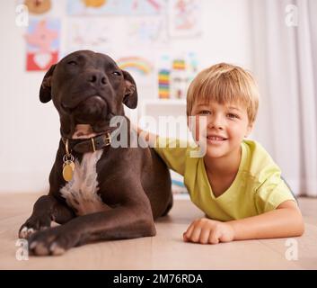 Er ist mein bester Freund. Ein kleiner Junge, der mit seinem Hund in seinem Zimmer spielt. Stockfoto