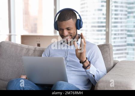 Ein glücklicher Afrikaner beginnt mit der Videokonferenz, sitzt auf dem Sofa mit einem Laptop Stockfoto