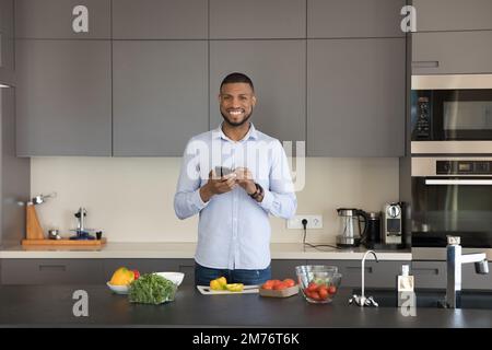 Mann steht in der Küche mit Smartphone-Lächeln schaut in die Kamera Stockfoto