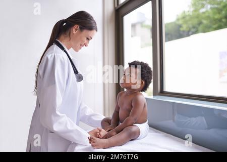 Gerade in für eine routinemäßige pädiatrische Untersuchung. Eine weibliche Kinderärztin, die eine Untersuchung an einem entzückenden kleinen Jungen macht. Stockfoto