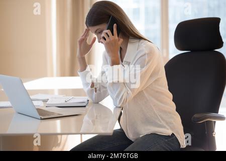 Eine Geschäftsfrau, die am Schreibtisch sitzt und ein unangenehmes Gespräch am Handy führt Stockfoto