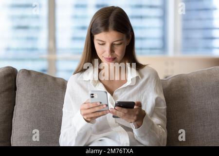 Eine Frau mit zwei modernen Smartphones, die auf der Couch sitzt Stockfoto