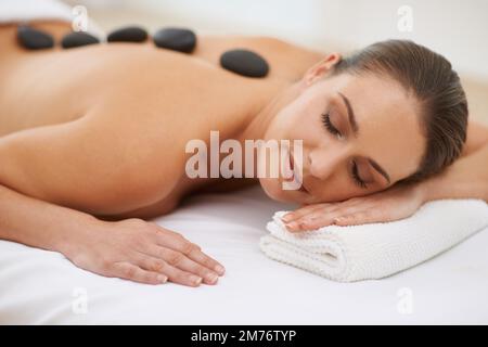 Im Spa stoned zu werden. Eine wunderschöne junge Frau, die eine Hot-Stone-Massage genießt. Stockfoto