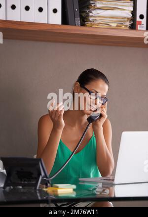 Sie ist fast eingeschlafen und hörte die Musik, während sie in der Warteschleife war. Eine hübsche junge Frau, die an ihrem Schreibtisch sitzt und telefoniert. Stockfoto