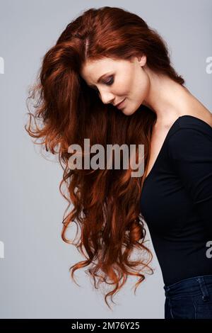 Los, lass deine Haare runter. Studioaufnahme einer jungen Frau mit schönen roten Haaren, die vor einem grauen Hintergrund posiert. Stockfoto