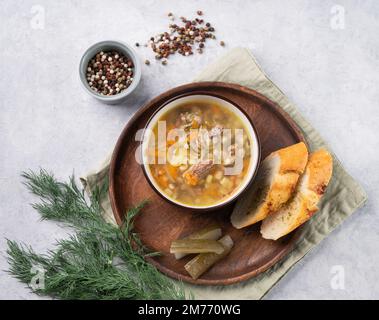 Traditionelle russische Suppe mit eingelegten Gurken. Gurke mit Perlgerste und Fleisch auf hellem Hintergrund mit frischem Dill, Gewürzen und Knoblauchbaguette. Stockfoto