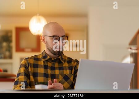 Heimbüro. Porträt eines jungen Weißen mit Brille, der am Laptop arbeitet. Konzept von Fernarbeit und Freiberufler. Stockfoto