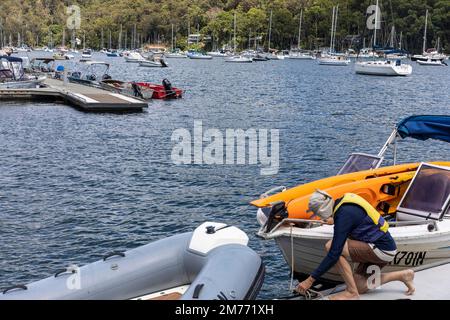 Der Mann sichert sein kleines Motorboot am Pier am Church Point Commuer Wharf, Pittwater, Sydney, Australien, mit einem Seil um die Stange Stockfoto