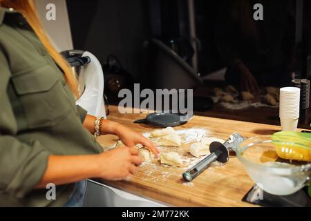 Hände einer Frau, die ein Stück rohen Teigs hält. Teig mit dem Messer in Stücke schneiden. Kochen in der Küche. Stockfoto