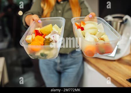 Frauenhände halten transparente Kunststoffbehälter mit Lebensmitteln und Gemüse, selektiver Fokus. Aufbewahrungsboxen für Lebensmittel. Stockfoto