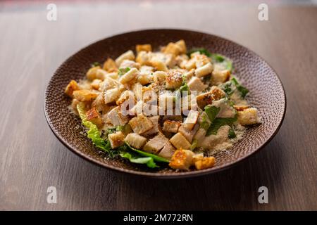 Teller mit köstlichem caesar-Salat mit Huhn, geriebenem Käse und knusprigen Crackern auf Tischhintergrund. Servieren Sie einen köstlichen Salat zum Essen Stockfoto