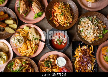 Tisch voller köstlicher europäischer Speisen in Tellern mit Blick von oben. Pommes Frites, Suppe, Salat, Burger, Nudeln, Saucen auf festlichem Dinner für große Veranstaltungen. Viele Gerichte Stockfoto