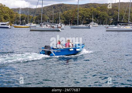 Vater und zwei Kinder in einem kleinen Polycraft-Shuttle-Boot auf Pittwater, von Church Point aus gesehen, Yachten im Hintergrund, Sydney, NSW, Australien Stockfoto