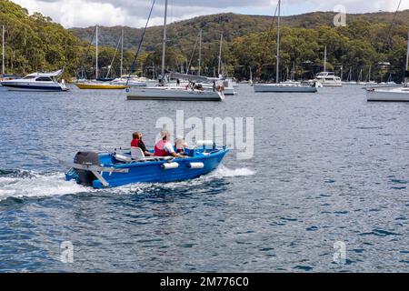 Vater und zwei Kinder in einem kleinen Polycraft-Shuttle-Boot auf Pittwater, von Church Point aus gesehen, Yachten im Hintergrund, Sydney, NSW, Australien Stockfoto