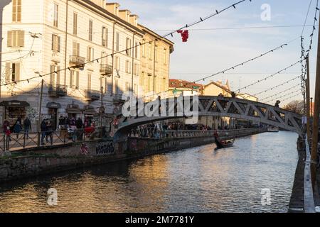 Mailand, Italien-Januar 05,2023: Gondelboot im Kanal, Menschen spazieren entlang des Ufers des Naviglio Milanese Kanals und entspannen in den Pubs, Mailand, Italien. Stockfoto