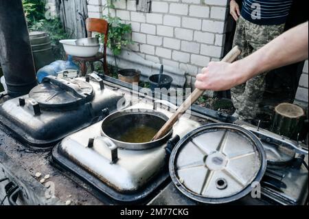 Ein Mann bereitet das Mittagessen in einer Militärküche zu, einem großen Holzspachtel zum Rühren von Essen. Stockfoto