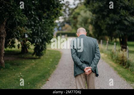 Ein Blick von hinten auf einen älteren Mann im Anzug, der auf einem Parkpfad läuft Stockfoto