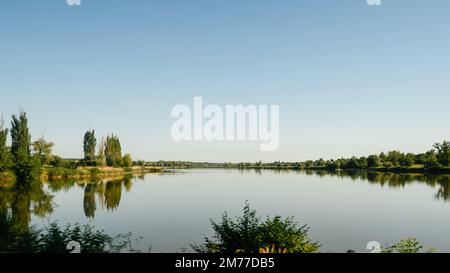 Großer See am Horizont mit Bäumen und Schilf, tiefblaues Wasser im See. Stockfoto