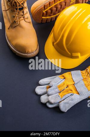 Arbeitsschutzkleidung Bauhelm Arbeitshandschuhe Arbeitsstiefel auf schwarzem Hintergrund Stockfoto