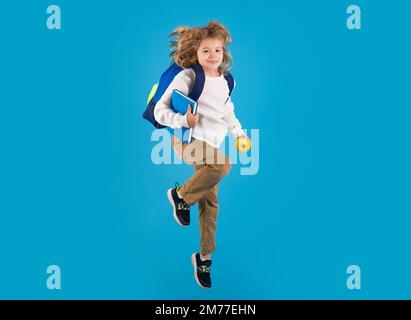 Kind springt und genießt die Schule. Schulkind in Schuluniform mit Rucksack und Kugelsprung. Schulkinder, die auf isoliertem blauem Hintergrund springen. Stockfoto