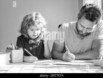 Bärtiger Vater schreibt Schulaufgaben mit seinem Sohn im Klassenzimmer, Bildung Stockfoto