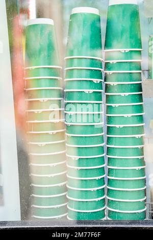 Viele grüne Einweg-Kaffeebecher aus Pappkaffee in Stapeln hinter dem Glas Stockfoto